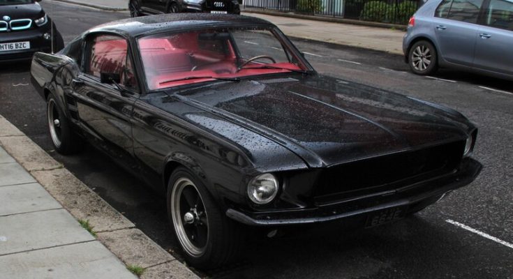 Black 1967 Ford Mustang parked on a wet street