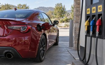 Red Japanese-style sport coupe beside a gasoline pump displaying 87, 89 and 93 octane options.