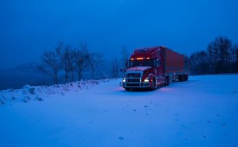 Red semi-truck parked on a snow-covered highway at blue hour