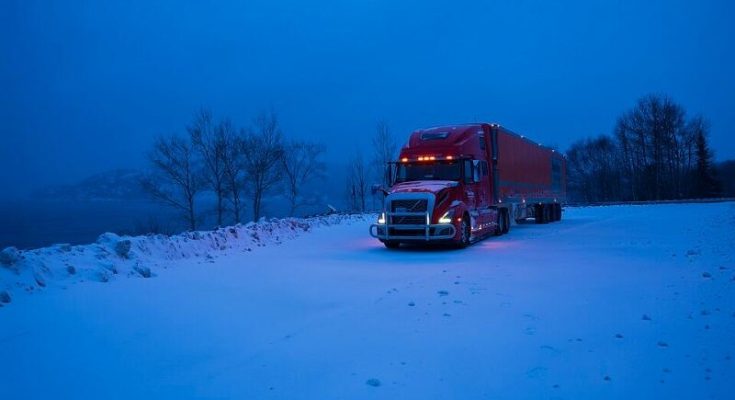 Red semi-truck parked on a snow-covered highway at blue hour